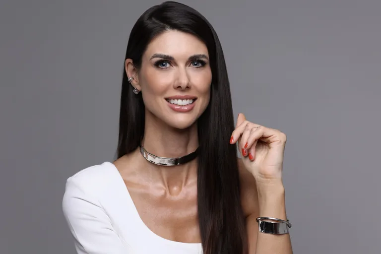 Dra. Monique Bins sorrindo, com blusa branca, em retrato profissional